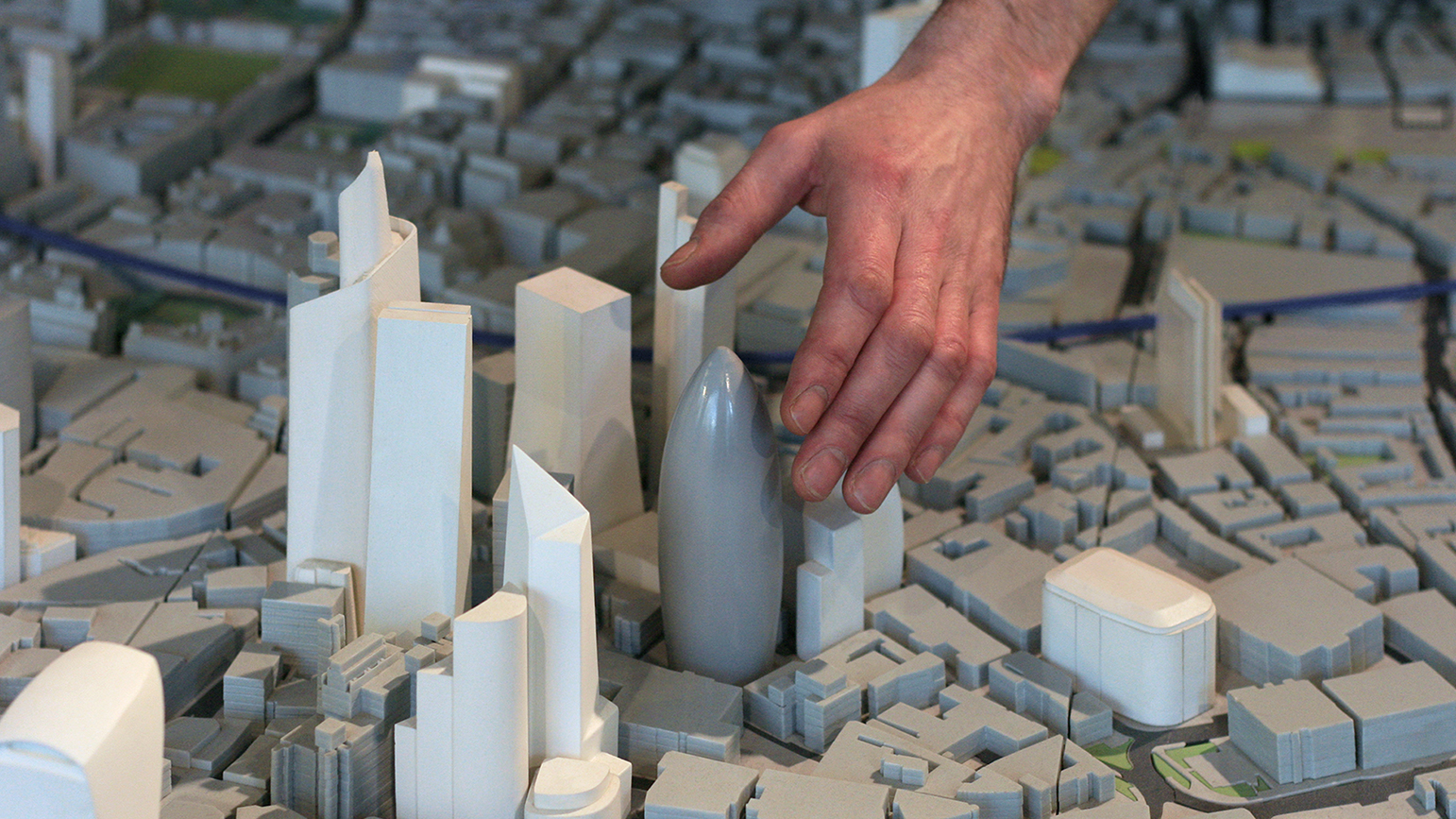 An image of a hand reaching down into a small-scale model city