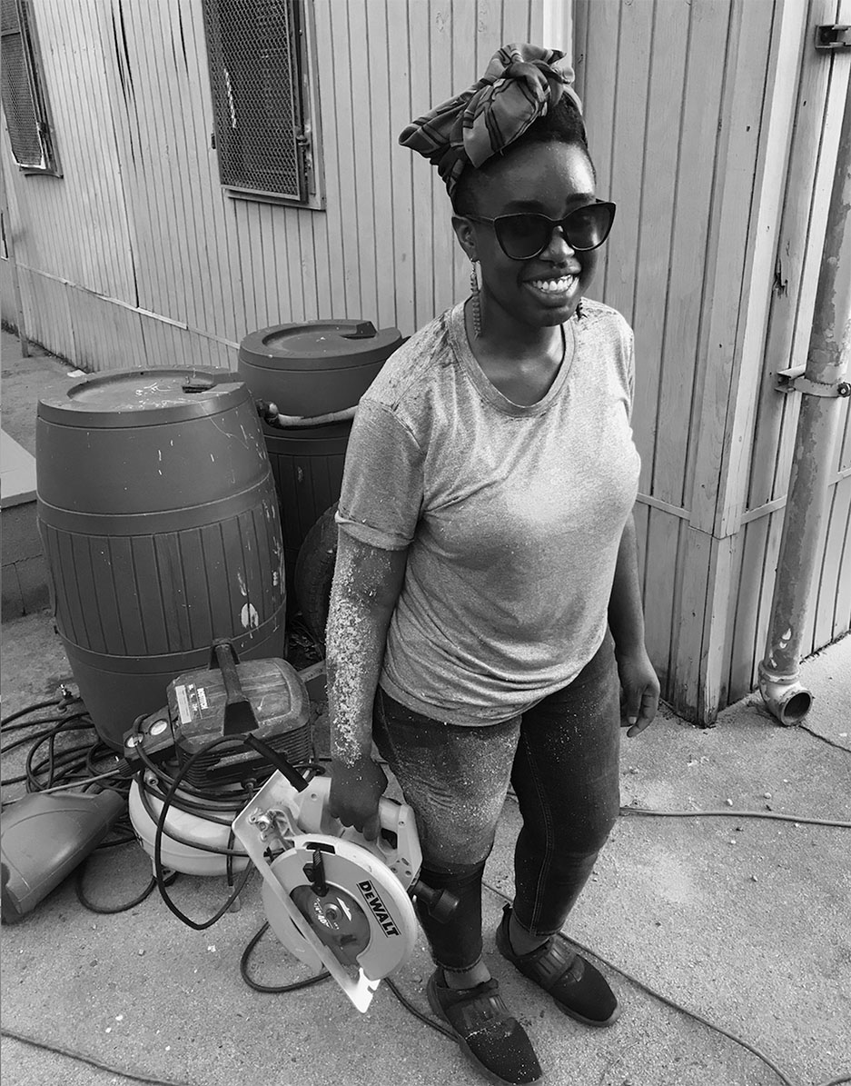Black and white photograph of a woman holding a circular saw and smiling at the camera