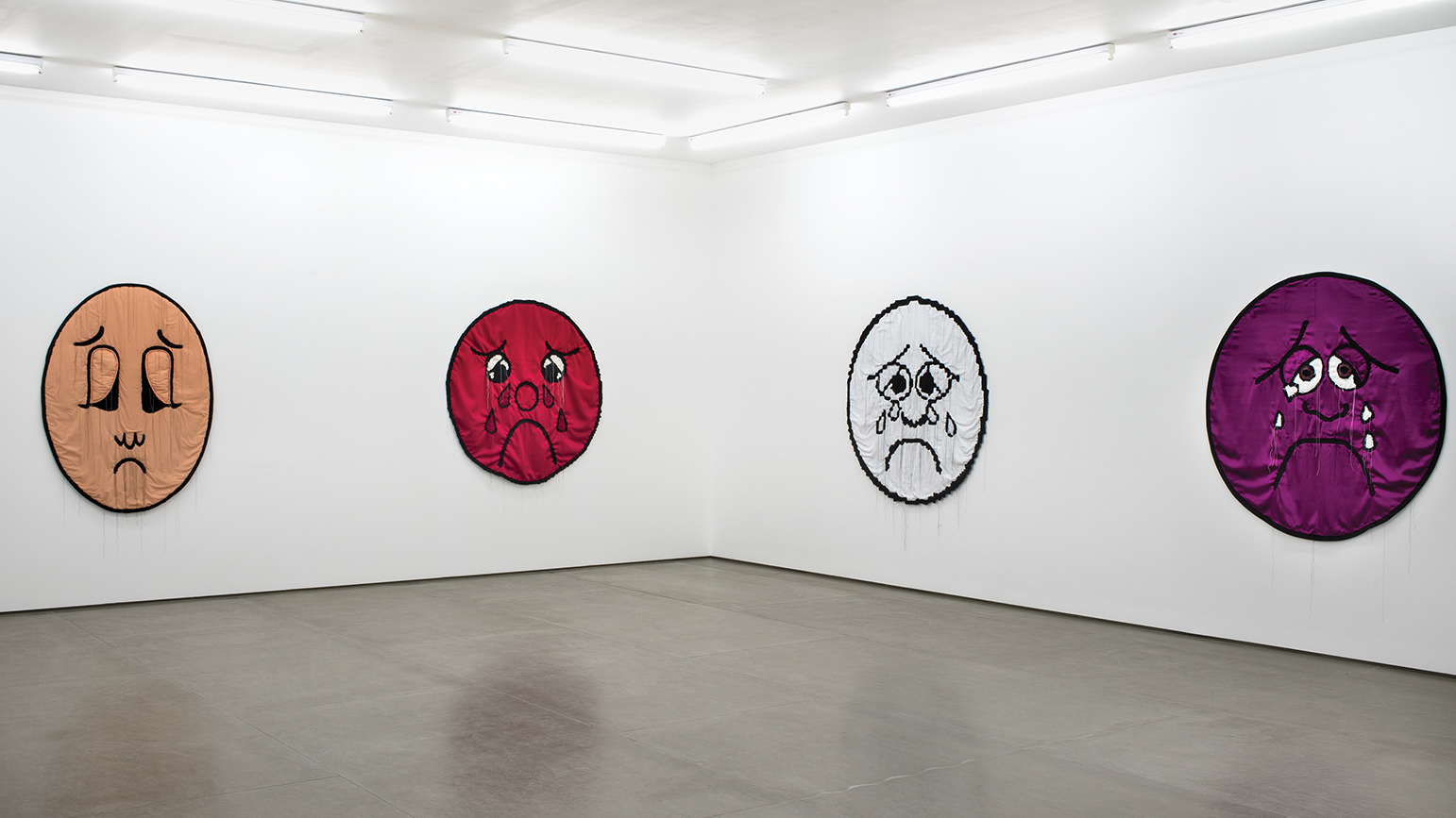 Gallery installation view with four large pain-scale faces constructed from fabric