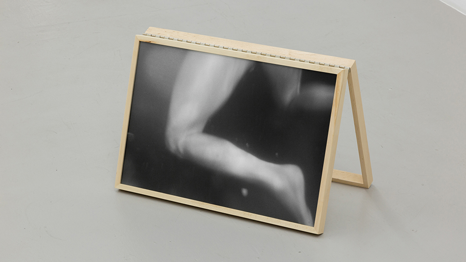 Black and white photograph of legs swimming, installed on a simple wooden easel on a gallery floor