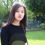Photograph of Hannah Kim standing outside on a sunny day with a green lawn and trees behind her