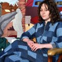 Photograph of Miranda Miller in a denim patchwork jumper in front of her family stories quilt